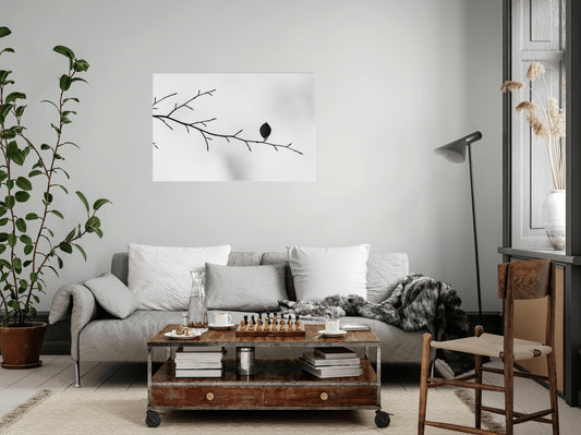 A styled living room featuring a square black and white wall art print of a leaf on a branch, hung above a gray sofa with white pillows and a wooden coffee table.