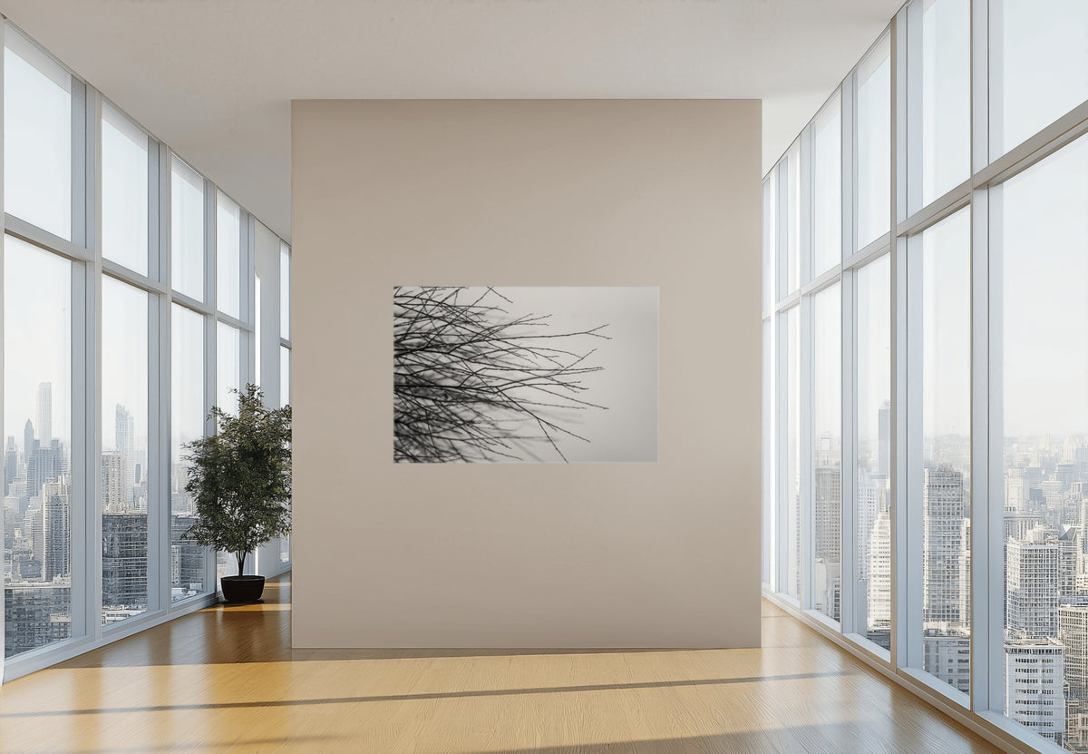 A framed black and white abstract wall art print featuring branching tree-like lines, displayed on a beige wall in a modern, sunlit room with large windows overlooking a city skyline.
