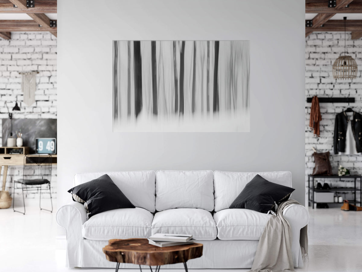 A large black and white vertical forest silhouette canvas print hanging on a white wall above a white sofa in a modern, stylishly decorated living room.